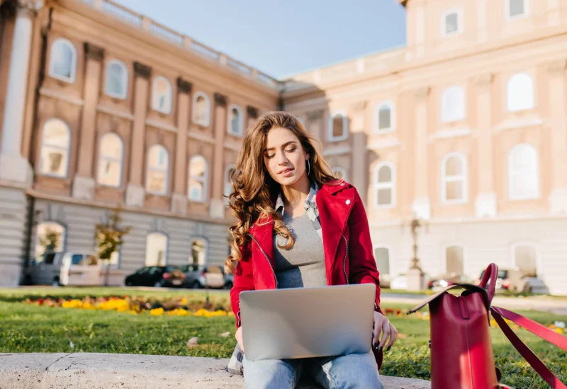outdoor-portrait-serious-curly-female-student-sitting-with-laptop-ground